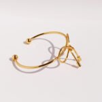 Wholesale bow knot bracelet with polished 8-shape twist design in 18K gold plated brass – sweet cool fashion cuff from JuneJewelry.com.