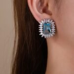 Wholesale blue gemstone earrings with a zircon sunburst on rhodium plated copper and 925 sterling silver pins from JuneJewelry.com – elegant fashion jewelry for bulk orders.