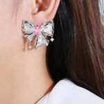 Wholesale pink bow stud earrings with white and pink cubic zirconia on a platinum plated copper base with a 925 silver needle from JuneJewelry.com.