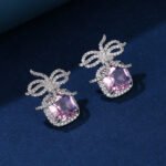 Wholesale zircon bow earrings with a cushion-cut pink center stone and cubic zirconia accents, platinum plated with a 925 silver needle, from JuneJewelry.com.