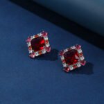 Wholesale ruby red gemstone stud earrings with a zircon cluster on rhodium plated copper and 925 sterling silver pins from JuneJewelry.com – elegant fashion jewelry for bulk orders.