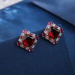 Wholesale ruby red gemstone stud earrings with a zircon cluster on rhodium plated copper and 925 sterling silver pins from JuneJewelry.com – elegant fashion jewelry for bulk orders.