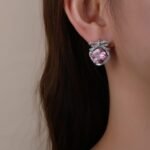 Wholesale pink zircon bow earrings with a central pink stone and cubic zirconia accents, platinum plated on a copper base with a 925 silver needle, from JuneJewelry.com.