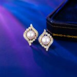 Wholesale Gold Swirl Pearl CZ Set (Necklace & Earrings) displayed on a blue background. The set features a white pearl surrounded by a gold-plated, waterdrop-shaped frame paved with sparkling Cubic Zirconia stones.