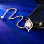 Wholesale Gold Swirl Pearl CZ Set (Necklace & Earrings) displayed on a blue background. The set features a white pearl surrounded by a gold-plated, waterdrop-shaped frame paved with sparkling Cubic Zirconia stones.