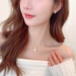 Wholesale Gold Swirl Pearl CZ Set (Necklace & Earrings) displayed on a blue background. The set features a white pearl surrounded by a gold-plated, waterdrop-shaped frame paved with sparkling Cubic Zirconia stones.