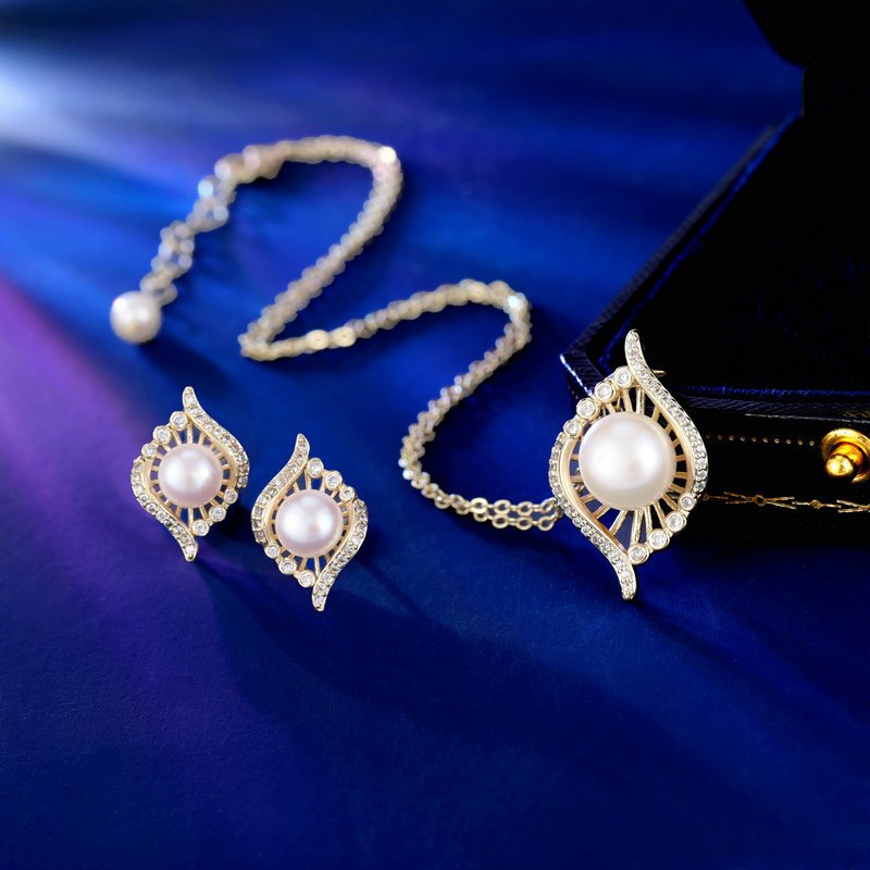 Wholesale Gold Swirl Pearl CZ Set (Necklace & Earrings) displayed on a blue background. The set features a white pearl surrounded by a gold-plated, waterdrop-shaped frame paved with sparkling Cubic Zirconia stones.