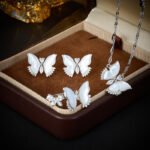 Wholesale Butterfly Shell Jewelry Set shown in gold and silver colors. The elegant set includes a butterfly pendant necklace, stud earrings, and an adjustable ring, all featuring iridescent Mother of Pearl wings and micro-paved Cubic Zirconia accents.