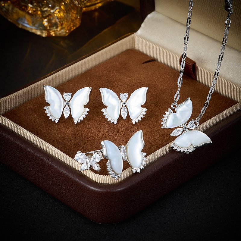 Wholesale Butterfly Shell Jewelry Set shown in gold and silver colors. The elegant set includes a butterfly pendant necklace, stud earrings, and an adjustable ring, all featuring iridescent Mother of Pearl wings and micro-paved Cubic Zirconia accents.