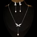 Wholesale Butterfly Tassel Pearl CZ Set in a platinum-plated finish on a black display bust. Features a matching necklace and drop earrings, both in a delicate butterfly shape with paved wings, ending in an elegant pearl tassel/drop.
