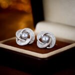 Wholesale Twist Knot Pearl CZ Set featuring a ring, stud earrings, and necklace pendant. Each piece showcases a dark gray pearl surrounded by a knot twist of micro-pave cubic zirconia baguette stones, set against a dark background in a jewelry box.