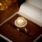 Wholesale Halo Pearl CZ Jewelry Set displayed in a box, showing a ring, stud earrings, and a pendant necklace. The design features a large round imitation pearl encircled by a halo of glittering cubic zirconia. Available in Golden Pearl/Yellow Gold and Black Pearl/Platinum finishes.