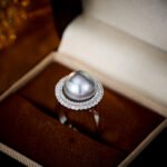 Wholesale Halo Pearl CZ Jewelry Set displayed in a box, showing a ring, stud earrings, and a pendant necklace. The design features a large round imitation pearl encircled by a halo of glittering cubic zirconia. Available in Golden Pearl/Yellow Gold and Black Pearl/Platinum finishes.