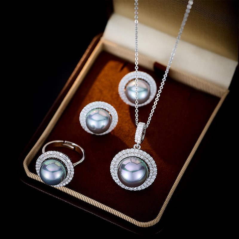 Wholesale Halo Pearl CZ Jewelry Set displayed in a box, showing a ring, stud earrings, and a pendant necklace. The design features a large round imitation pearl encircled by a halo of glittering cubic zirconia. Available in Golden Pearl/Yellow Gold and Black Pearl/Platinum finishes.
