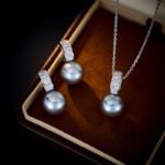 Wholesale Simple Baguette Pearl Set on a white background, featuring a necklace and drop earrings. Both pieces showcase a round dark gray pearl suspended from a rectangular bail fully paved with Baguette-Cut Cubic Zirconia.