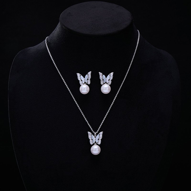 Wholesale Butterfly Pearl CZ Set in both white gold and yellow gold plating. Features a Micro-Pave CZ butterfly motif suspending a round imitation pearl, available as a necklace and matching earrings.