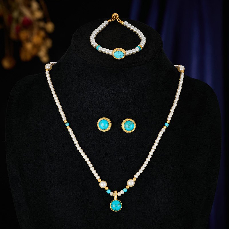 Wholesale Turquoise Pearl Beaded Set on a white background. Includes a long necklace with a round turquoise-colored pendant, matching gold-textured stud earrings, and an adjustable pearl slider bracelet.