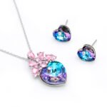 Swarovski Element crystal jewelry set featuring a heart pendant and stud earrings, crowned with a cluster of pear-cut crystals, shown in pink-purple/blue and sapphire blue/white variations.