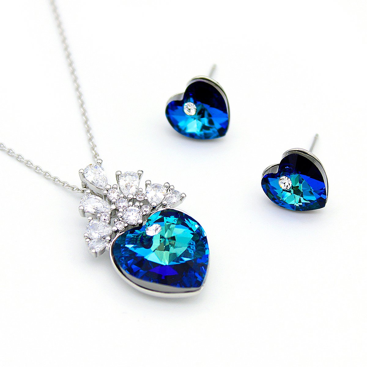 G100749E18A.154.A Swarovski Element crystal jewelry set featuring a heart pendant and stud earrings, crowned with a cluster of pear-cut crystals, shown in pink-purple/blue and sapphire blue/white variations.