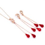 Wholesale red crystal tassel jewelry set in rose gold plating with a knot pendant and long dangle earrings with red crystal teardrops from JuneJewelry.com – unique and high-quality.