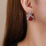 Wholesale red ribbon earrings with green zircons and 925 silver needles from JuneJewelry.com – unique bow-knot fashion jewelry for bulk buyers.