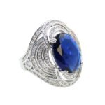 Wholesale blue zircon ring with oval-cut center stone and tiered halo design on gold plated copper from JuneJewelry.com – adjustable cocktail jewelry for bulk orders.