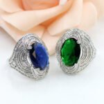 Wholesale blue zircon ring with oval-cut center stone and tiered halo design on gold plated copper from JuneJewelry.com – adjustable cocktail jewelry for bulk orders.