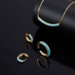 Niche light luxury geometric turquoise jewelry set wholesale displaying a micro-pave turquoise-blue curved bar smile necklace, matching huggie hoop earrings, and an open adjustable ring on junejewelry.com