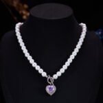 Light luxury ice-cracked zircon heart pearl jewelry set wholesale featuring a classic round pearl strand necklace with a front-facing OT toggle clasp, a micro-pave halo peach heart pendant, and matching pearl-topped drop earrings from junejewelry.com