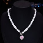 Light luxury ice-cracked zircon heart pearl jewelry set wholesale featuring a classic round pearl strand necklace with a front-facing OT toggle clasp, a micro-pave halo peach heart pendant, and matching pearl-topped drop earrings from junejewelry.com
