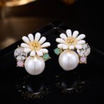 Gold-plated flower stud earrings featuring a white enamel daisy blooming over a smooth faux pearl, accented with a faceted crystal, turquoise bead, and lavender stone.