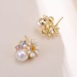 Gold-plated flower stud earrings featuring a white enamel daisy blooming over a smooth faux pearl, accented with a faceted crystal, turquoise bead, and lavender stone.