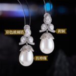 Tear-shaped pearl drop earrings featuring three teardrop crystal clusters top and micro-pavé cap accents, available in gold and palladium plating.