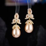 Tear-shaped pearl drop earrings featuring three teardrop crystal clusters top and micro-pavé cap accents, available in gold and palladium plating.