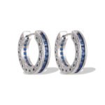 Sapphire blue huggie hoop earrings featuring channel-set princess-cut blue cubic zirconia, side filigree lattice detailing, and platinum plating.