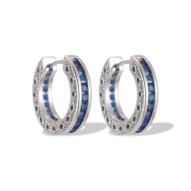 Sapphire blue huggie hoop earrings featuring channel-set princess-cut blue cubic zirconia, side filigree lattice detailing, and platinum plating.