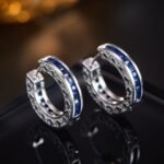 Sapphire blue huggie hoop earrings featuring channel-set princess-cut blue cubic zirconia, side filigree lattice detailing, and platinum plating.
