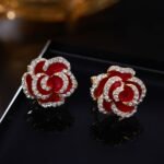 Layered enamel rose clip-on stud earrings featuring clear rhinestone-rimmed petals in rich red and classic black enamel finishes.