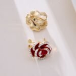 Layered enamel rose clip-on stud earrings featuring clear rhinestone-rimmed petals in rich red and classic black enamel finishes.