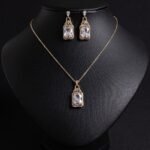 Niche emerald cut zircon halo jewelry set wholesale featuring a rectangular emerald-cut main gem inside an intricate pave cubic zirconia filigree frame with matching drop earrings from junejewelry.com
