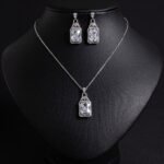 Niche emerald cut zircon halo jewelry set wholesale featuring a rectangular emerald-cut main gem inside an intricate pave cubic zirconia filigree frame with matching drop earrings from junejewelry.com