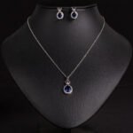 Niche crown zircon halo pendant necklace earring set wholesale featuring a micro-pave crown bail suspending a halo-set round crystal pendant with matching stud earrings from junejewelry.com