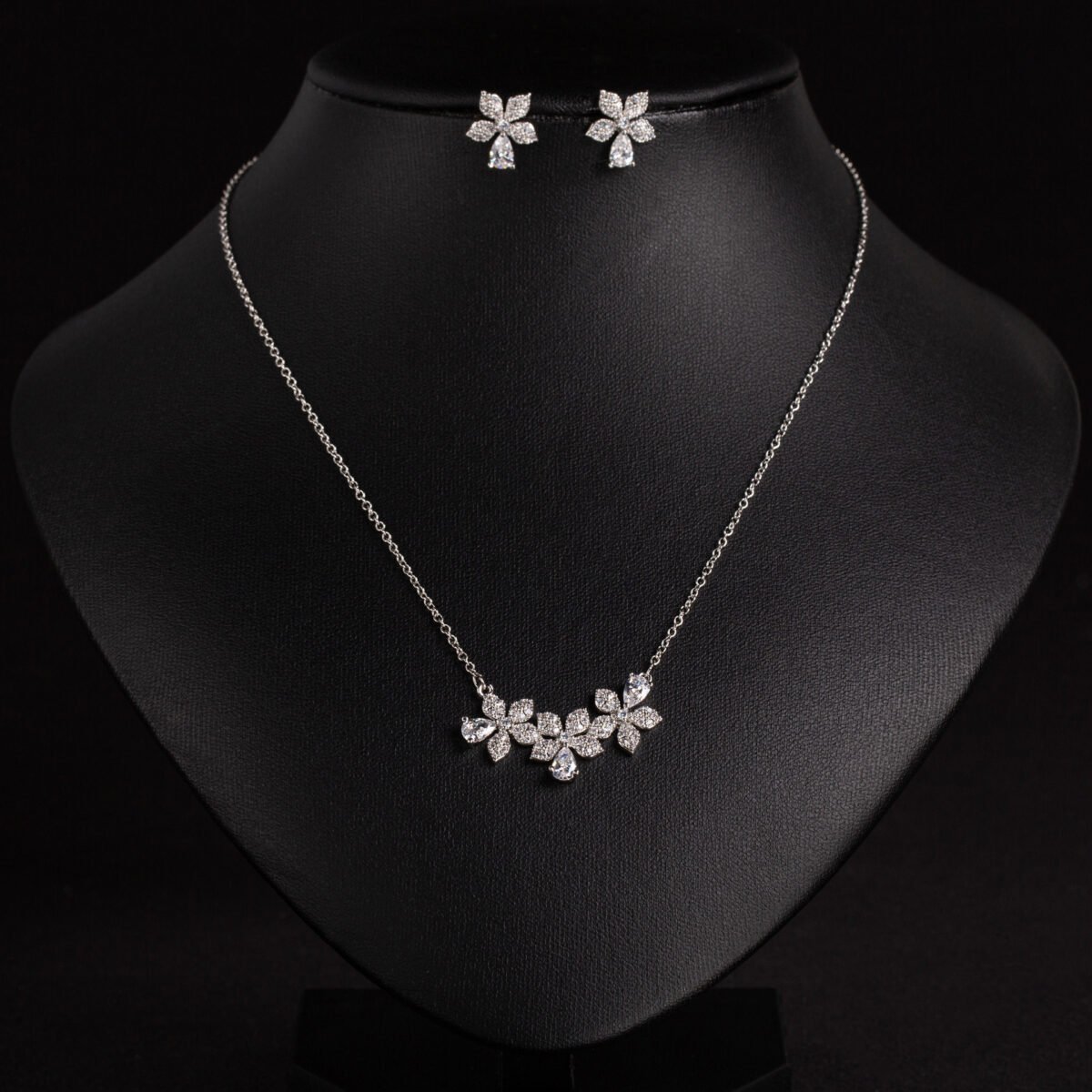 Niche triple flower crystal jewelry set wholesale featuring a curved garland of pave CZ flowers with teardrop crystal accents and matching floral stud earrings from junejewelry.com