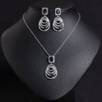 Niche concentric ring drop zircon jewelry set wholesale featuring an emerald-cut halo crystal suspended above tiered concentric pave rings with matching drop earrings from junejewelry.com