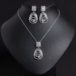 Niche concentric ring drop zircon jewelry set wholesale featuring an emerald-cut halo crystal suspended above tiered concentric pave rings with matching drop earrings from junejewelry.com