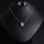 Niche bow heart crystal jewelry set wholesale featuring a delicate pave CZ bow ribbon knot topped heart crystal pendant chain necklace and matching stud earrings from junejewelry.com