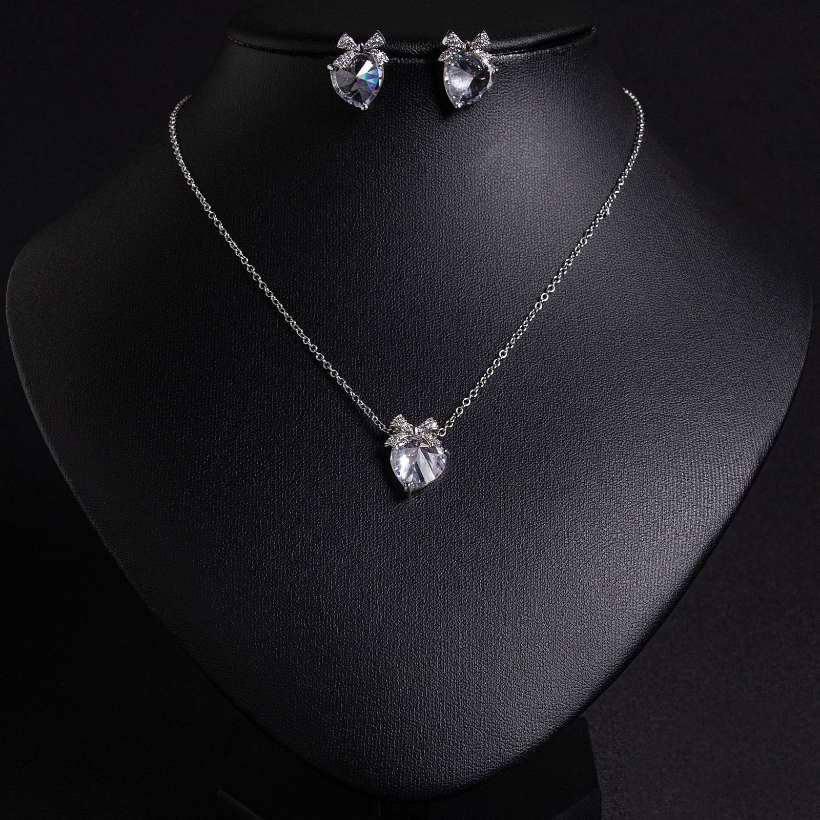 LJT89650 (2) Niche bow heart crystal jewelry set wholesale featuring a delicate pave CZ bow ribbon knot topped heart crystal pendant chain necklace and matching stud earrings from junejewelry.com