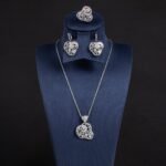Niche swirl heart crystal jewelry set wholesale featuring an openwork filigree swirl heart pendant necklace, statement ring, and matching drop earrings studded with cubic zirconia from junejewelry.com