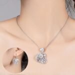 Niche swirl heart crystal jewelry set wholesale featuring an openwork filigree swirl heart pendant necklace studded with cubic zirconia and matching drop earrings from junejewelry.com