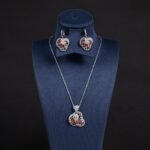 Niche swirl heart crystal jewelry set wholesale featuring an openwork filigree swirl heart pendant necklace studded with cubic zirconia and matching drop earrings from junejewelry.com